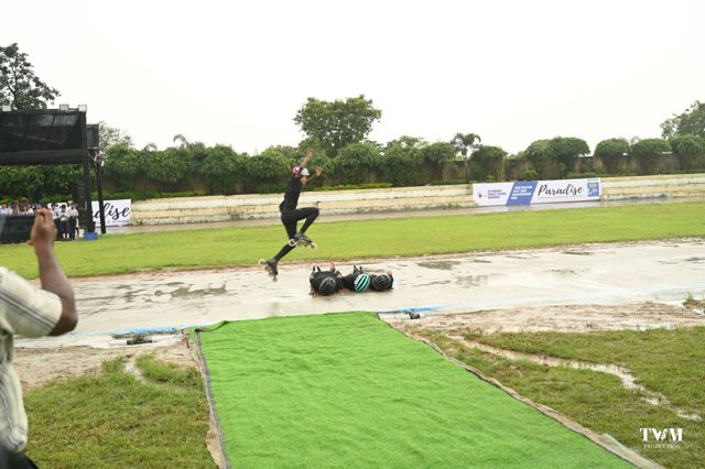 A skater in black leaping over three skaters lying on the track during a display