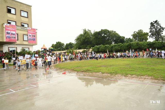 Teams from many schools marching past with flags and name boards beside the school building