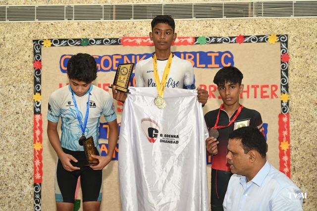 Three medallists on the podium holding trophies in front of a decorated board
